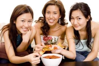 Three young women dipping chips into a bowl of salsa