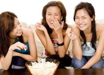 Three young women holding popcorn and smiling