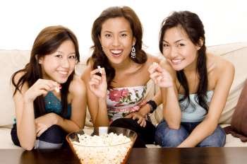 Three young women holding popcorn and smiling