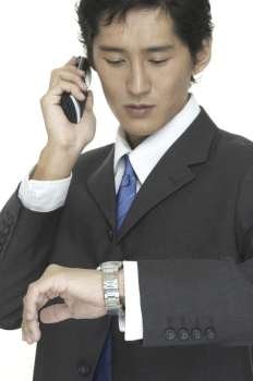 An asian businessman checks the time whilst talking on the phone