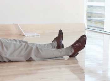 Legs of businessman as he lies down on the wooden floor, next to his white laptop