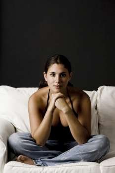 Young woman sitting on a couch with her hands on her chin