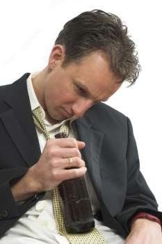 Man dressed in business attire sitting drunk with a beer bottle in his hand looking depressed