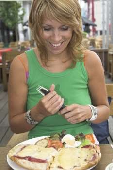 Pretty blond girl sitting outdoors on a terrace and looking very happy with her food that just arrived