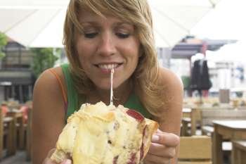 Pretty blond girl taking a bite out of her cheesy sandwich pulling the cheese into strings