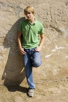 Attractive teen boy leaning against wall in sunlight.