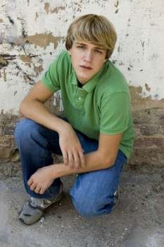 15 year old boy outside against old wall. Blonde hair, blue eyes.
