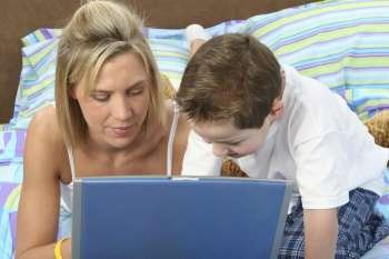 Mother and son in pajamas in bed working on laptop together. Ages 29 and 5.