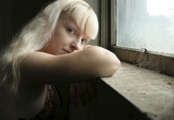 Beautiful German seventeen year old girl with head on window sill. Spiderwebs in window. Natural beauty - no make-up. Blonde hair, blue eyes.