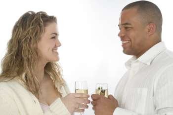 Young couple with champagne, smiling at each other. Shot in studio over white.