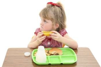 Little girl not happy with her school lunch. Adorable sad look on face while holding orange slice.