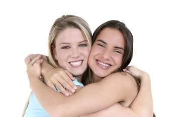 Two teen girls smiling and hugging over white background. 