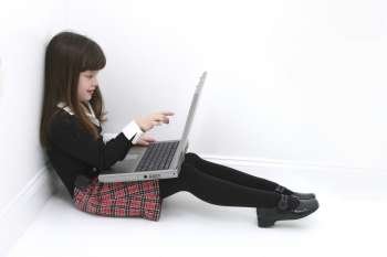 Beautiful little girl sitting in a corner of the room using a laptop. 
