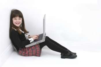 Beautiful little girl sitting in a corner of the room using a laptop. 