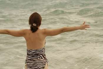 Woman looking at the ocean with her arms stretching