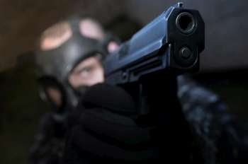 A guy wearing a gasmask is aiming seriously by his handgun.