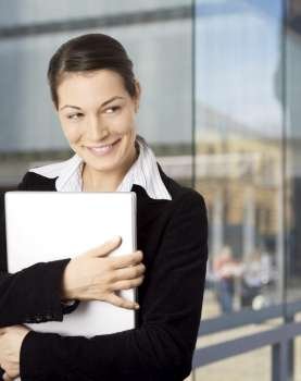 Young and happy businesswomen is posing with laptop in front of an officebuilding.
