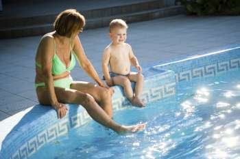 Grandmother and two years old granson enjoy water and sunshine on the poolside. Natural light, summer.