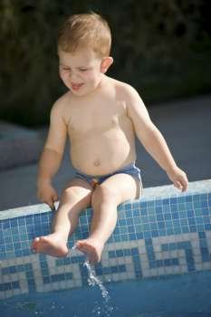 Two years old baby boy enjoys water and sunshine on the poolside. Natural light, summer.