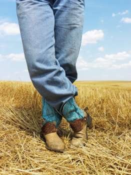 Cowboy standing in harvested crop field wearing funky cowboy boots.
