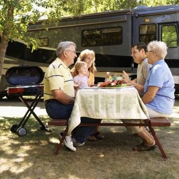 Three generation Caucasian family seated at picnic table in front of recreational vehicle talking.