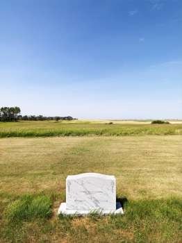 Cemetary headstone in rural field under blue sky.
