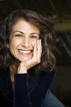 Portrait of pretty mid adult Caucasian woman smiling with head on hand making eye contact.