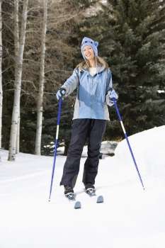 Mid adult Caucasian female skier wearing blue ski clothing standing on ski slope smiling.