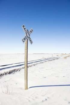 Railroad crossing sign by tracks in rural desolate snowy landscape.