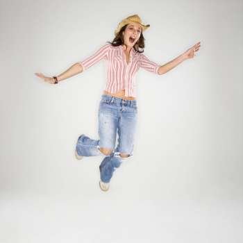 Young adult Caucasian woman wearing cowboy hat leaping into air with excited expression.