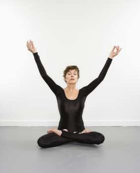Portrait of pretty Caucasian woman in spandex bodysuit sitting in meditation pose with arms raised.