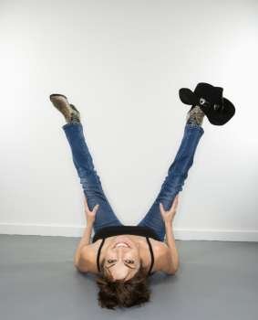 Fun portrait of smiling pretty Caucasian woman lying on back looking upside down with cowboy hat on foot.
