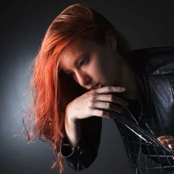 Pretty redhead young woman wearing leather jacket hanging over back of chair.