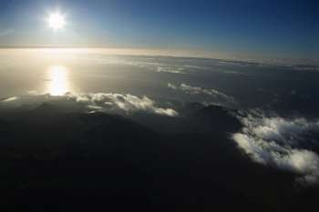 Aerial view of Maui, Hawaii coast with sun over Pacific ocean and mountainous landscape.
