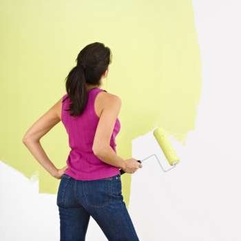 Woman standing and looking at partially painted wall holding paint roller.