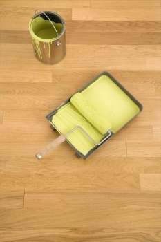 Still life of paint roller in tray with paint can on wood floor.