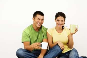 Couple sitting on floor drinking coffee and smiling.