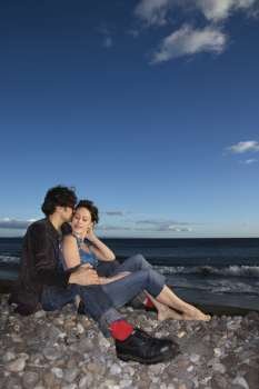 Caucasian young adult couple sitting close on beach.
