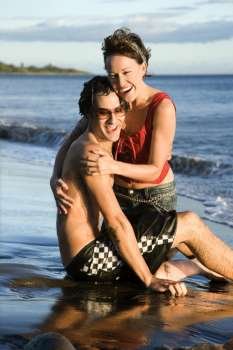 Caucasian young adult couple frolicking on beach.