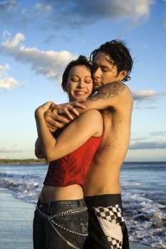 Young Caucasian adult couple embracing on beach.