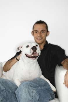 Young adult male Caucasian holding white Pit Bull dog on lap.