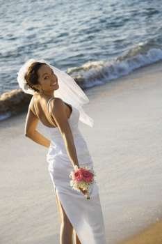 Young adult female Caucasian bride standing on beach.