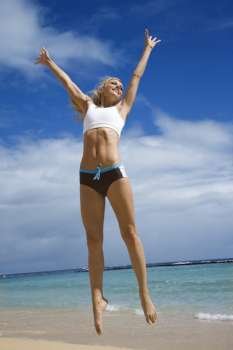 Caucasian young adult woman jumping on beach.