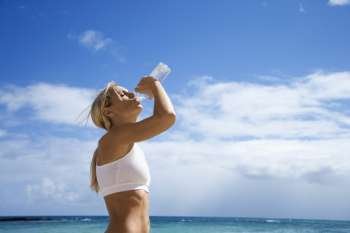 Caucasian young adult woman drinking water on beach.