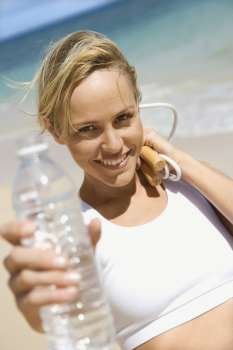 Caucasian young adult woman holding jump rope and water bottle on beach.