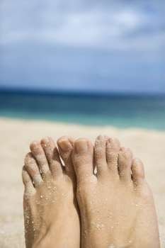 Caucasian young adult woman sandy feet on beach.