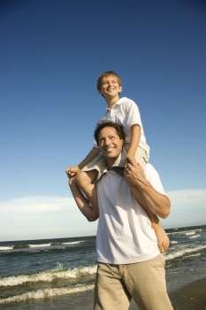Caucasian father with pre-teen boy on shoulders on beach.