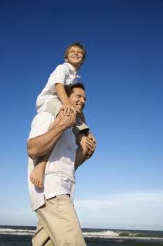 Caucasian father with pre-teen on shoulders on beach.