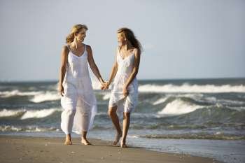 Caucasian mother and pre-teen girl walking on beach holding hands.