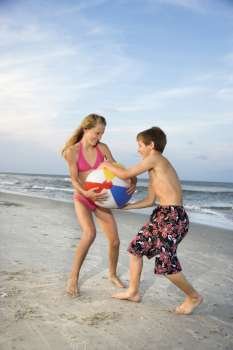 Caucasian pre-teen boy and girl pulling on beachball.